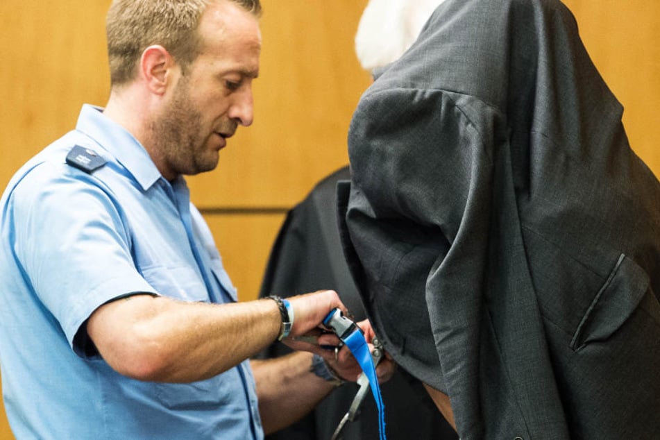 Ein Justizbeamter (l) öffnet die Handschellen des Angeklagte im Gerichtssaal.