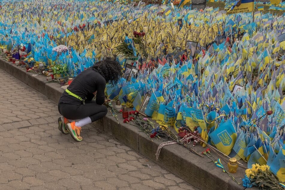 A woman reacts next to flags bearing symbols and colors of Ukraine set to commemorate fallen Ukrainian army soldiers at Independence Square in Kyiv.
