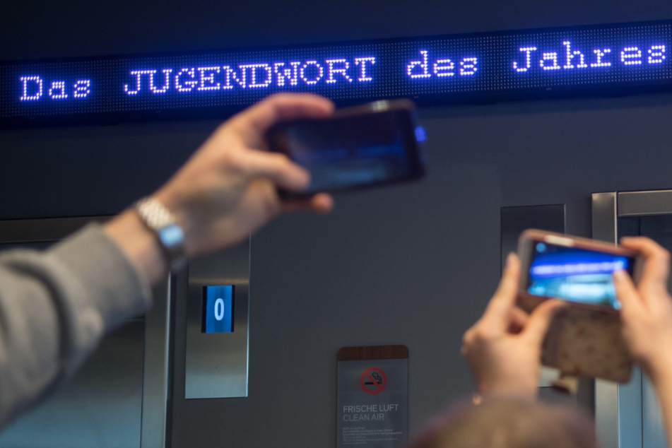 Auf einem Laufband erscheint "Jugendwort des Jahres" über den digitalen Newsticker eines Hotel.