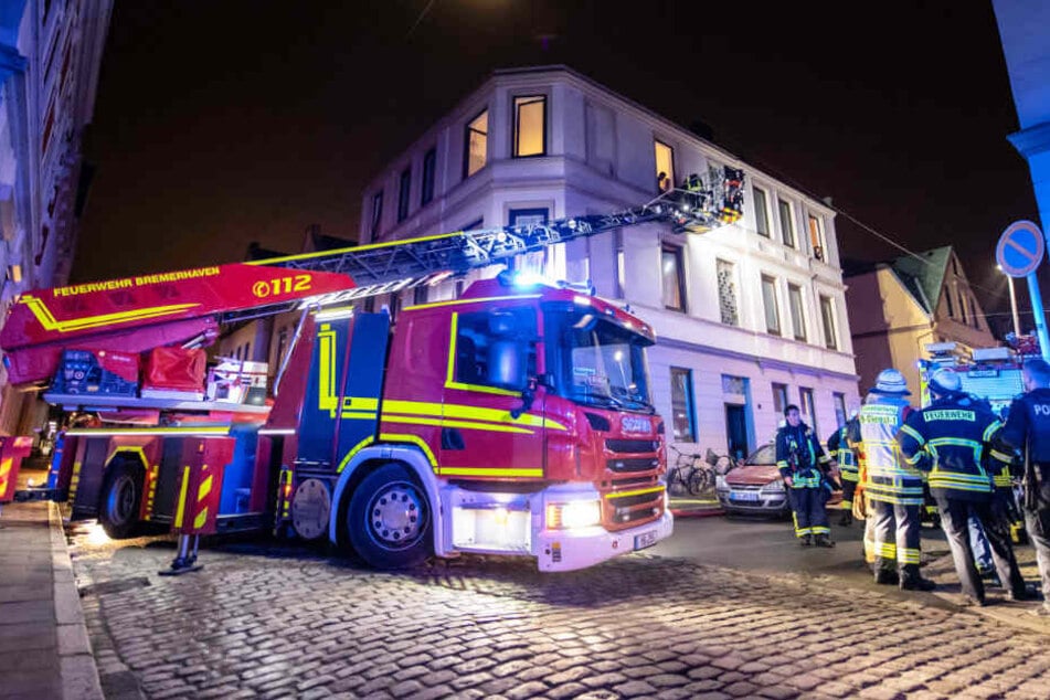 Feuerwehrleute löschen von einer Feuerwehrleiter aus einen Brand in einem Mehrfamilienhaus in Bremerhaven.
