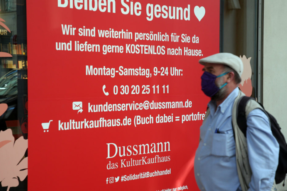 Ein Mann trägt einen Mundschutz und geht an einem Hinweisschild am für Kunden geschlossenen Kulturkaufhaus Dussmann in der Friedrichstraße vorbei.