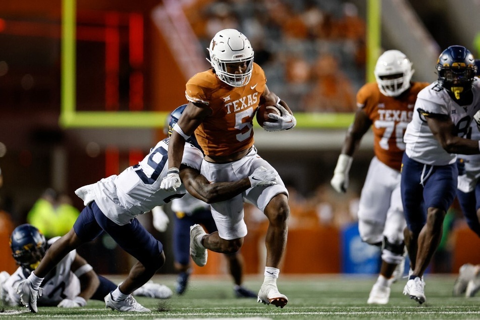 Bijan Robinson (c) of the Texas Longhorns runs the ball while defended by Mumu Bin-Wahad (l) of the West Virginia Mountaineers in the fourth quarter at Darrell K Royal-Texas Memorial Stadium.
