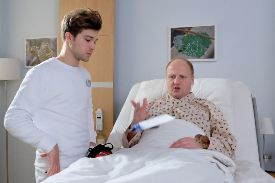 IaF-Folge 812: Kris Haas (Jascha Rust, l.) soll Patient Ole Beck (Christian Hockenbrink, r.) ein Langzeit-EKG anlegen. Doch der zeigt sich nicht gerade kooperativ.