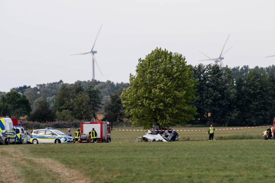 Einsatzkräfte der Feuerwehr und der Polizei stehen nach dem Absturz von einem Kleinflugzeug auf einem Feld zwischen dem Ortsteil Badingen und Gransee.