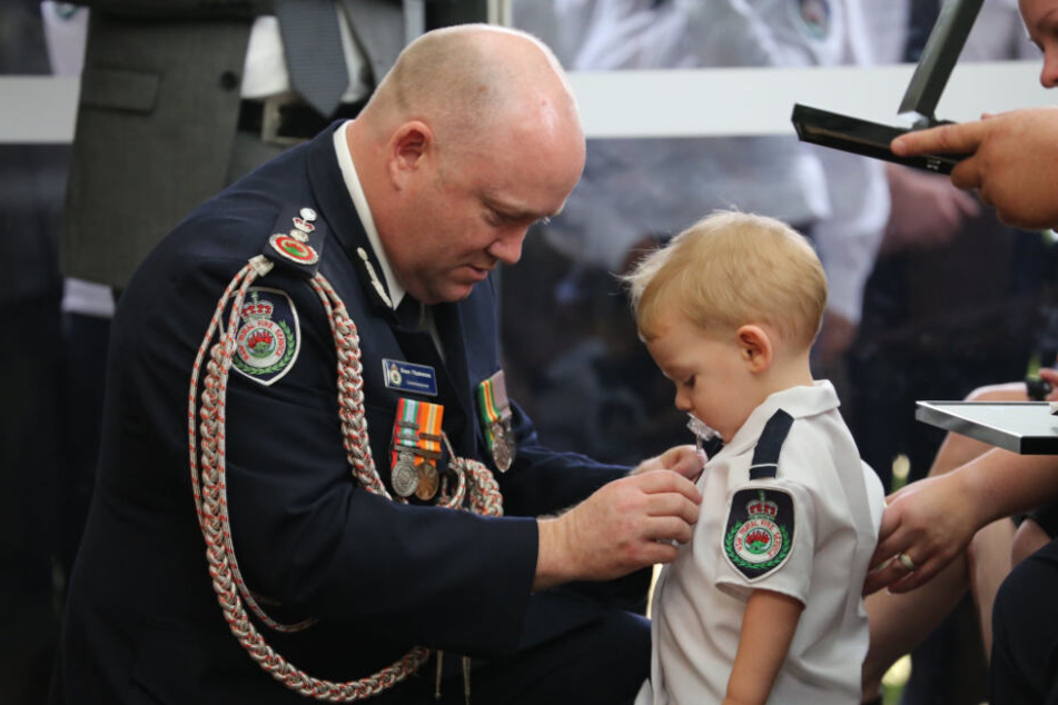 Kommissar Shane Fitzsimmons (l.) überreicht dem Sohn des freiwilligen Feuerwehrmannes Geoffrey Keaton bei dessen Beerdigung stellvertretend eine posthume Auszeichnung für seinen mutigen Einsatz.