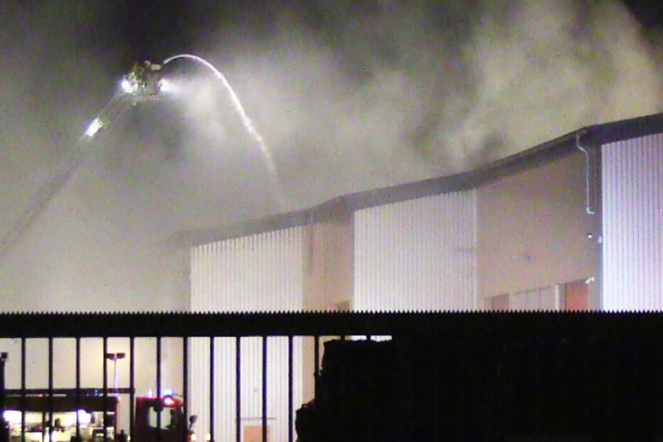 Feuerwehrleute löschen die brennende Halle mit Abfall.