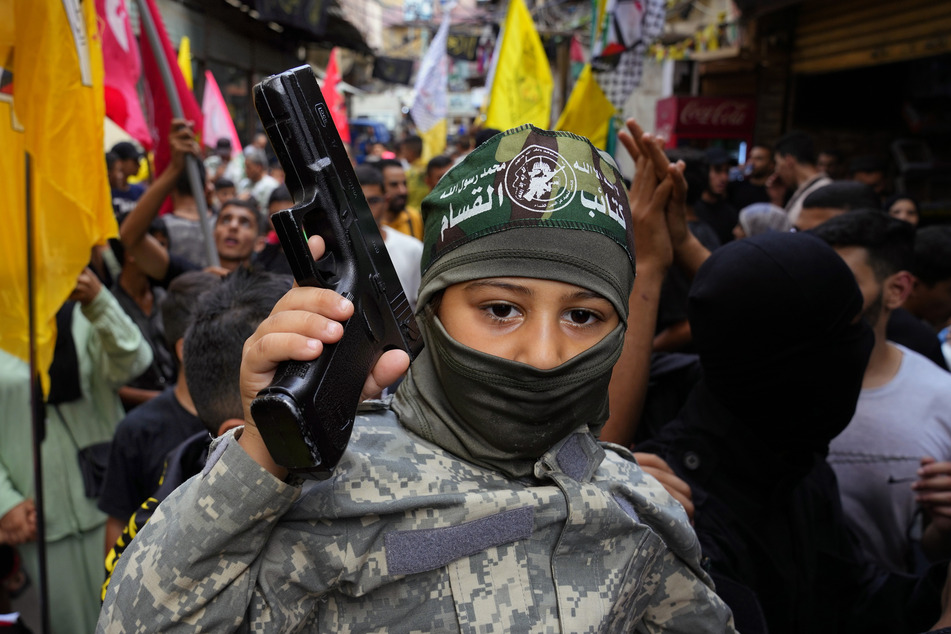 Bourj al-Barajneh, Libanon: Ein palästinensischer Junge in einer Armeeuniform hält eine Pistole in der Hand, während andere tanzen, um die Angriffe der militanten Hamas-Gruppe auf Israel zu feiern.
