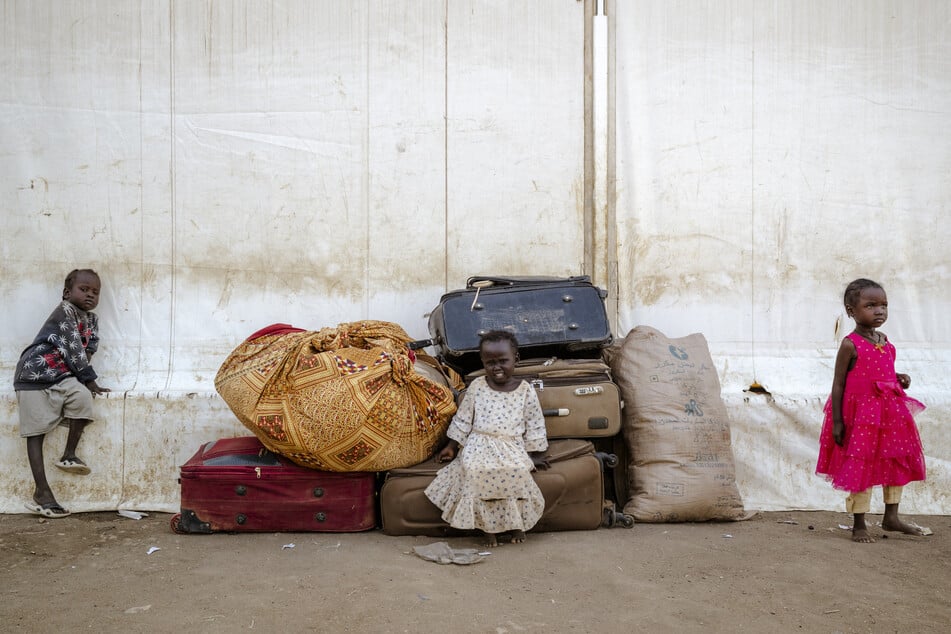 After fleeing Sudan, three young children sit in front of a pile of luggage at the Renk Transit Center in South Sudan on November 17, 2025.