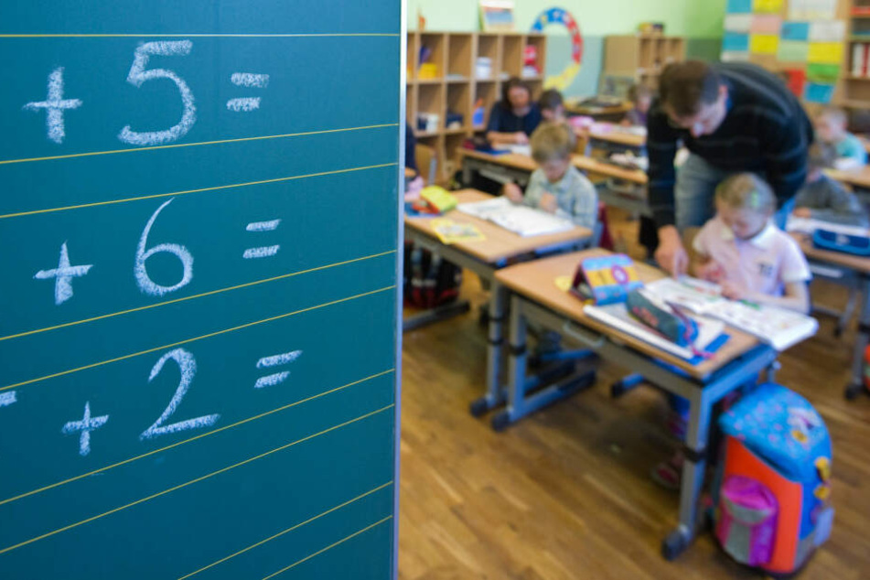 Ein Lehrer hilft einer Grundschülerin bei ihren Aufgaben. (Symbolbild)