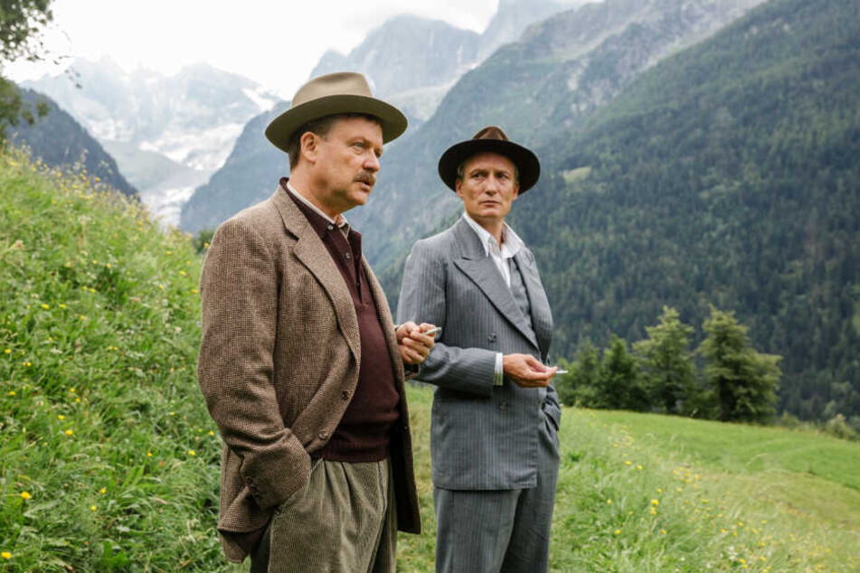 Julius (l., Justus von Dohnányi) und Arthur Kemper (Oliver Masucci) besprechen die schwere Lage vor den malerischen Schweizer Berglandschaften.