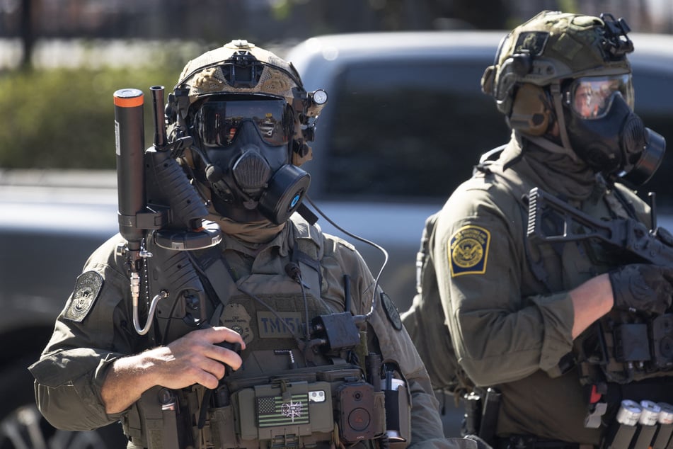 Federal law enforcement agents stand guard as they are confronted by community members and activists for reportedly shooting a woman in the Brighton Park neighborhood in Broadview, Illinois, on October 4, 2025.