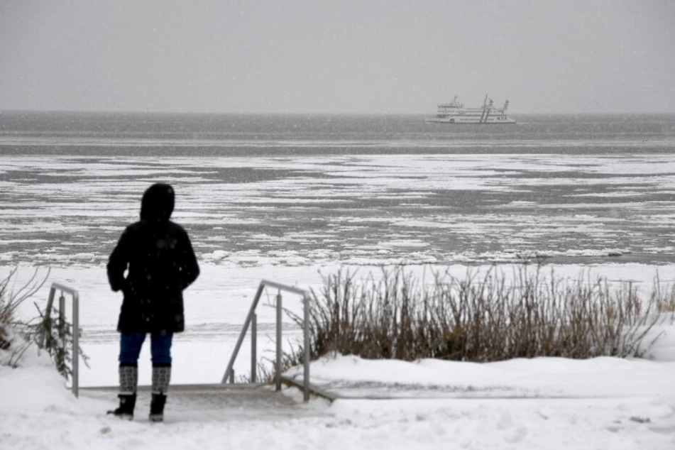 Eine Fußgängerin steht am Strand im Schnee. (Symbolbild)