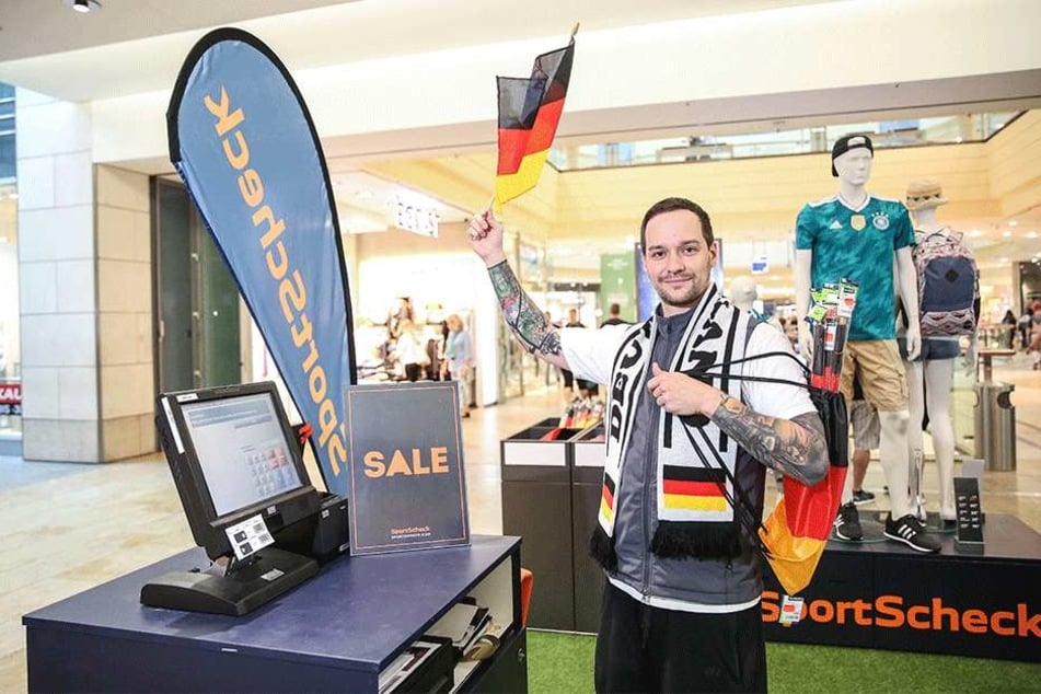 Sportscheck-Verkäufer Alex Böhm (29) hält die deutsche Fahne hoch. Das Geschäft in der Altmarkt-Galerie setzt bei Wimpeln, Beuteln, Schals und Co. auf Rabatte.