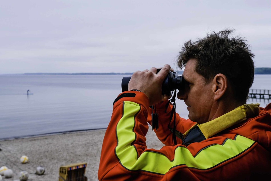 Ein DLRG-Retter schaut durch ein Fernglas auf die Ostsee hinaus. (Symbolbild)