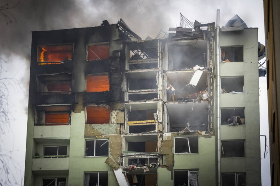 Ein Bewohner steht in einem oberen Stockwerk eines zwölfstöckigen Mehrfamilienhauses, das durch eine Gasexplosion schwer beschädigt wurde, und guckt nach unten.