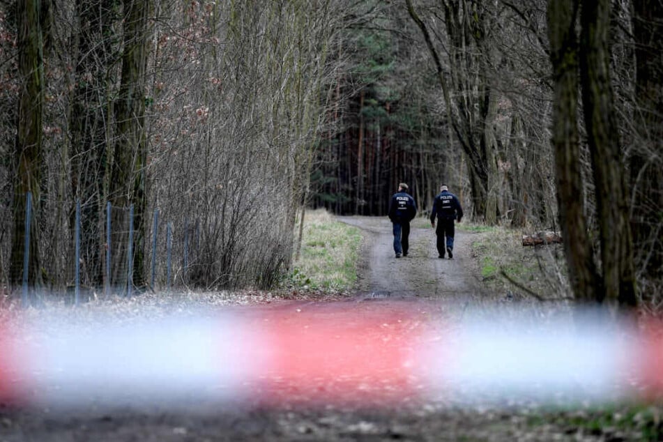 Polizisten gehen einen abgesperrten Waldweg in der Nähe des Fundortes der Leiche entlang. (Symbolbild)
