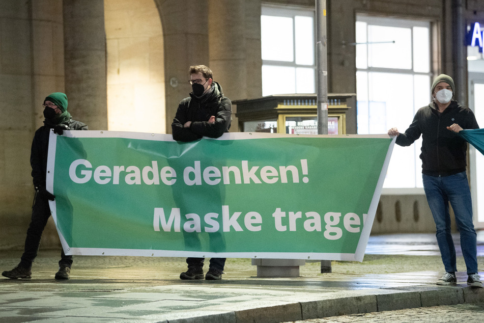 Gegendemonstranten halten am Dr.-Külz-Ring in Dresden ein Transparent mit der Aufschrift "Gerade denken! Maske tragen!" hoch.