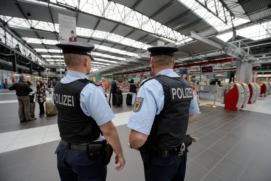 Zwei Beamte der Bundespolizei stehen am Flughafen Dresden International im Bereich des Check-in und beobachten die Reisenden.