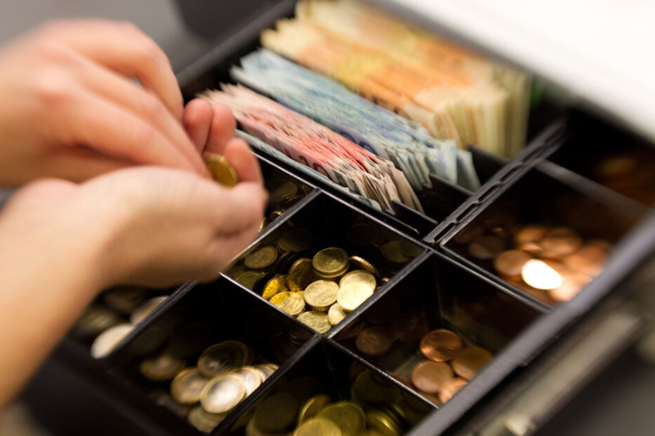Eine Kassiererin holt Geld aus der Kasse heraus. (Symbolbild)
