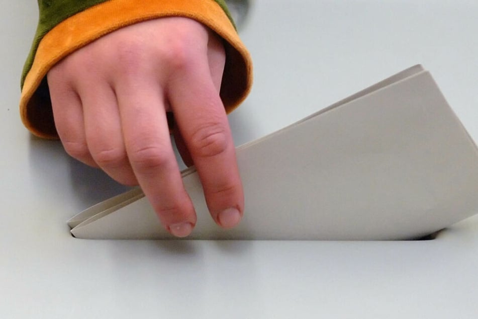 Eine jugendliche Hand steckt einen Stimmzettel in eine Wahlurne.