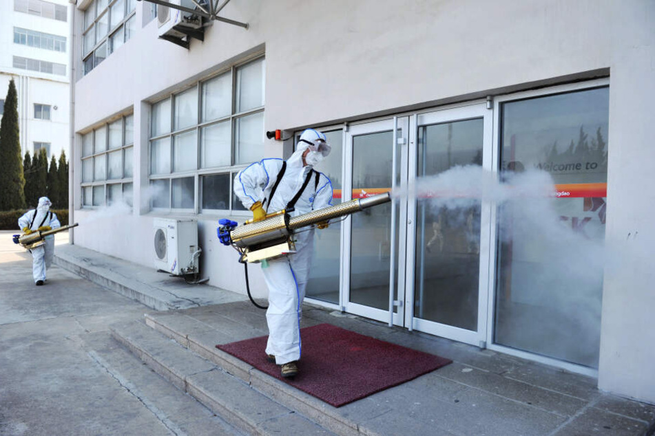 Arbeiter in Schutzkleidung sprühen mit Desinfektionsmittel vor einem Geschäft in China.