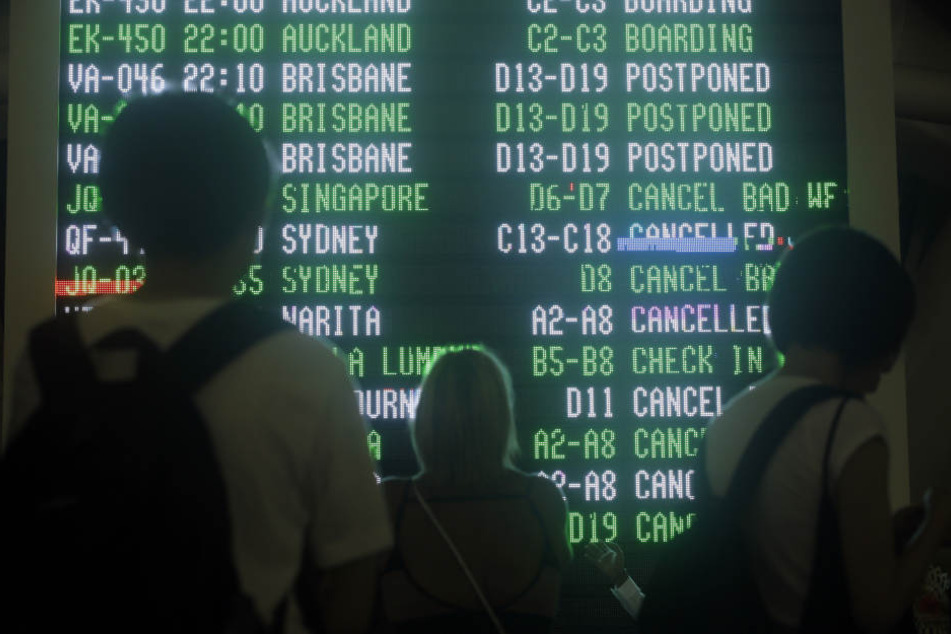 Passagiere schauen auf dem Internationalen Flughafen von Bali auf eine Anzeigetafel, die über zahlreiche ausgefallene Flüge informiert.