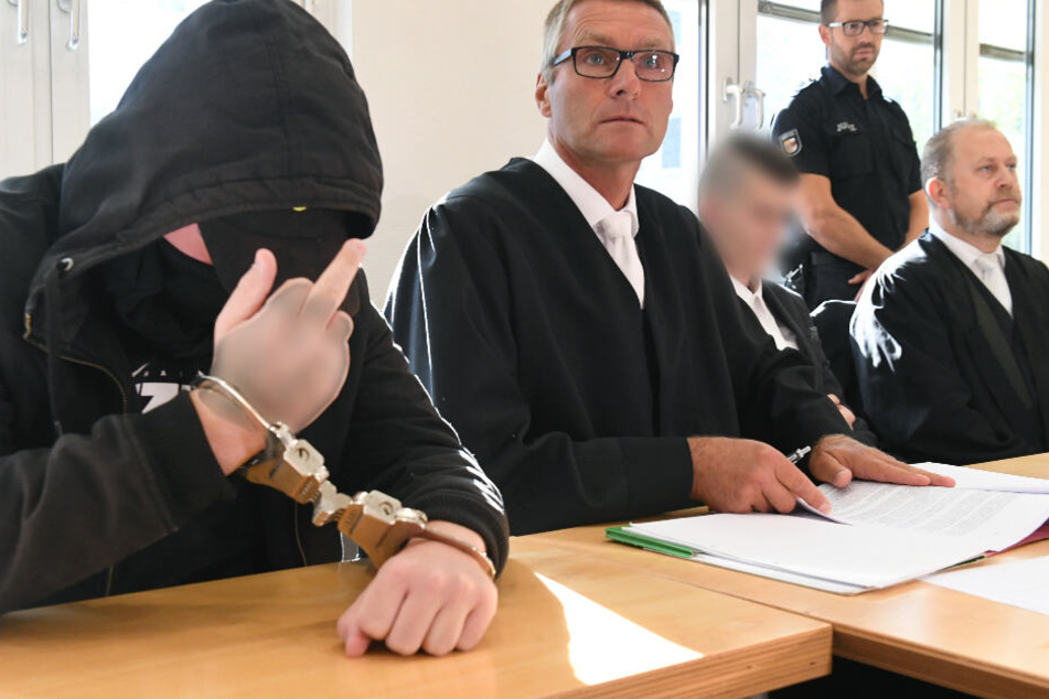 Der 19-jähriger Angeklagte (l) zeigt im Gerichtssaal im Landgericht den Mittelfinger.