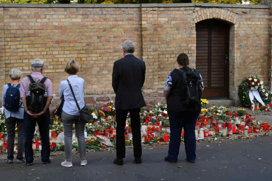 Menschen stehen in Halle nach dem rechtsextremistischen Anschlag vor niedergelegten Kerzen und Blumen an der Synagoge.