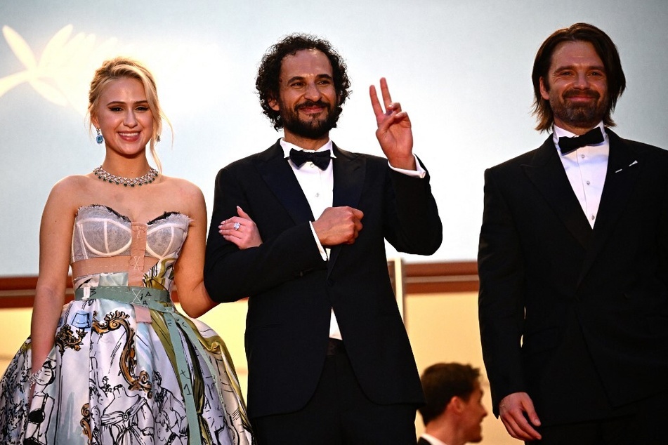 From l. to r.: Bulgarian actor Maria Bakalova, Iranian director Ali Abbasi, and Romanian-American actor Sebastian Stan smile to the crowd after the screening of The Apprentice at the Cannes Film Festival.