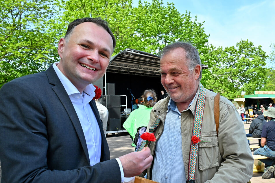 André Schollbach (44, Die Linke, l.) mit einer Mai-Nelke und Uli Reinsch (69), der die Blumen gegen eine Spende verteilt.