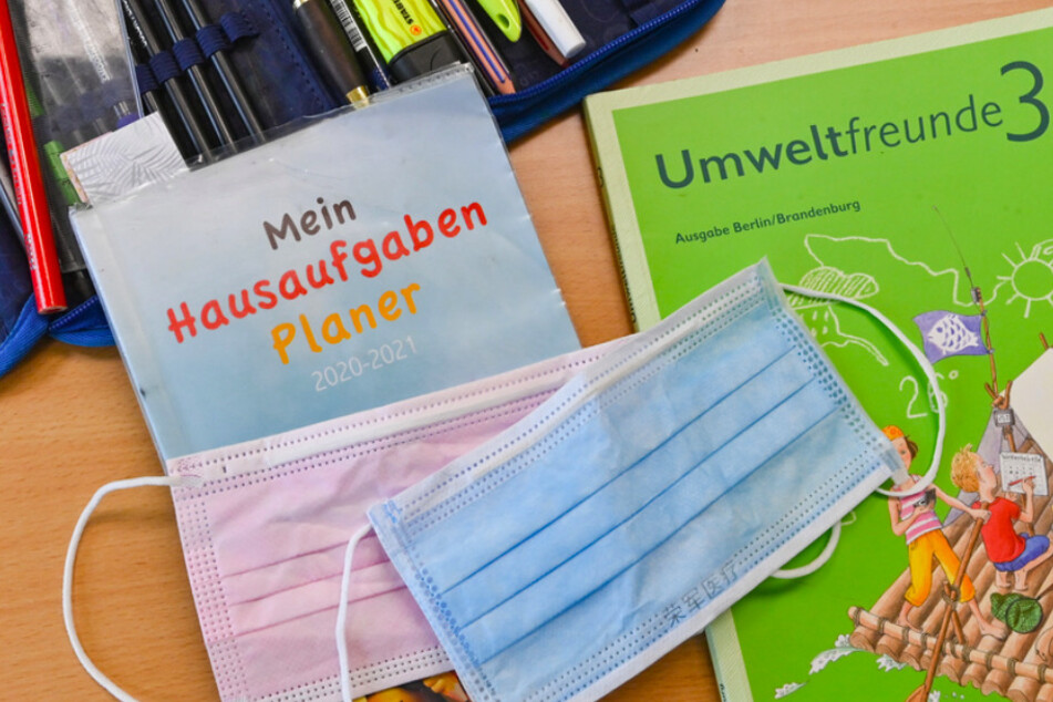 Masken liegen während einer Pause auf Arbeitsmaterialien eines Schülers in einem Klassenraum einer Grundschule.