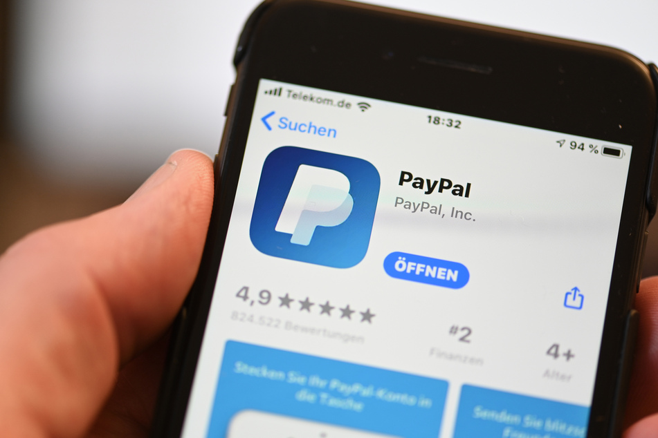 Die Applikation von PayPal ist auf einem Mobilfunkgerät zu sehen, das ein Mann in der Hand hält.