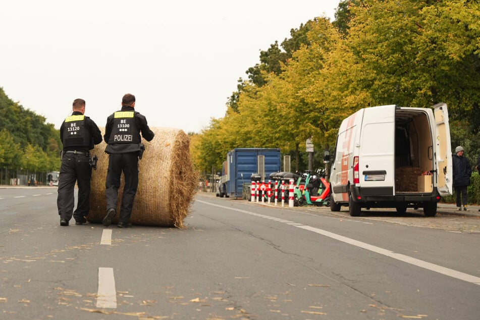 Zwei Polizisten rollen einen großen Strohballen von der Straße.