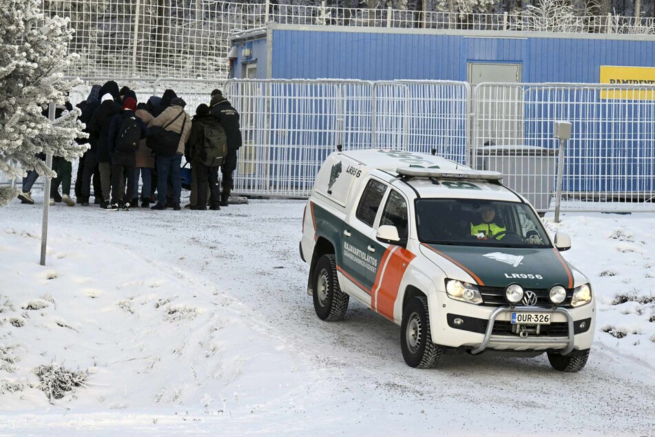 Flüchtlinge und ein Fahrzeug des finnischen Grenzschutzes stehen an einem Grenzübergang zwischen Finnland und Russland. Finnland will von Freitag an drei weitere Grenzübergänge nach Russland schließen.