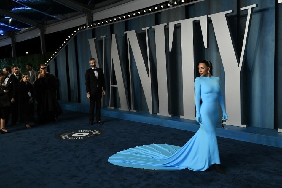 Kim Kardashian turned heads at the 2022 Oscar's after party with a stunning neon blue body-con Balenciaga gown - matched with gloves, a drastic train, black Knife boots, silver micro-shades, and crystal drop earrings.