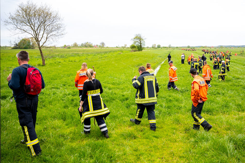 Feuerwehrleute suchen mit einer Menschenkette auf einem Feld nach dem vermissten Arian.