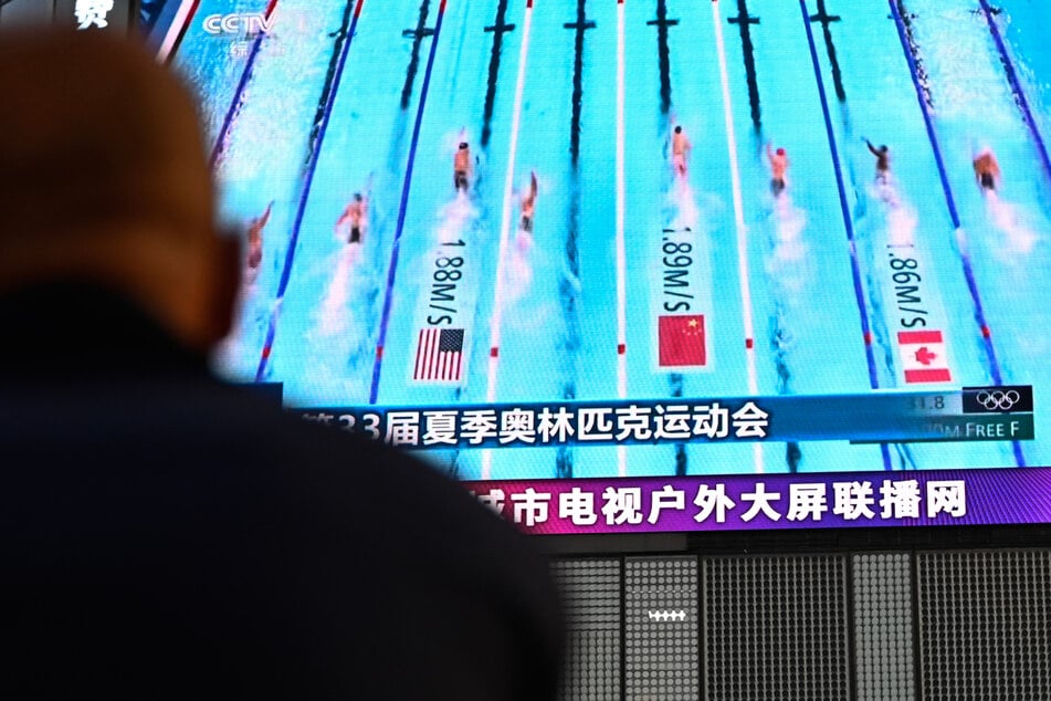 A man watches a screen showing news coverage of the Chinese team competing in the women's 4x100m freestyle relay event at the Paris 2024 Olympic Games at a mall in Beijing.