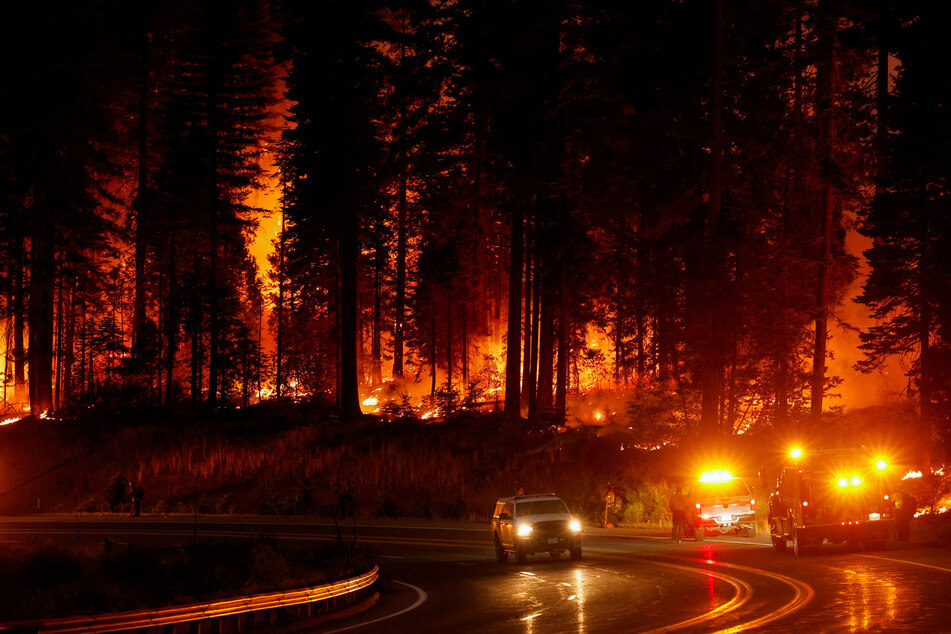 A vehicle passes firefighters standing by the road as the Park Fire burns, near Jonesville, California.