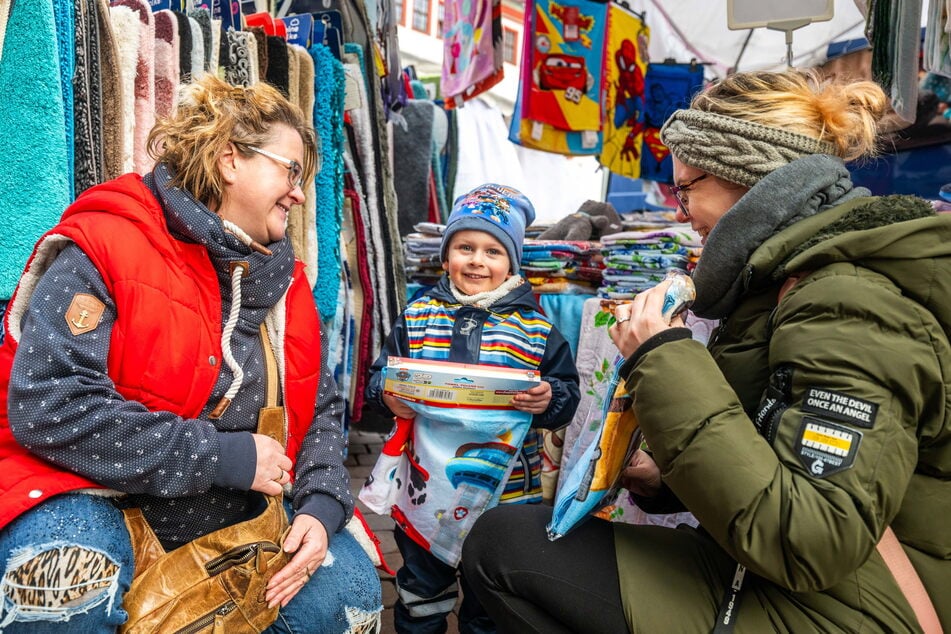 Lyam (2) und seine Mutter Mandy (35) kaufen am Stand von Sandra Claus-Riedel (50, l.) aus Hartenstein ein Handtuch.