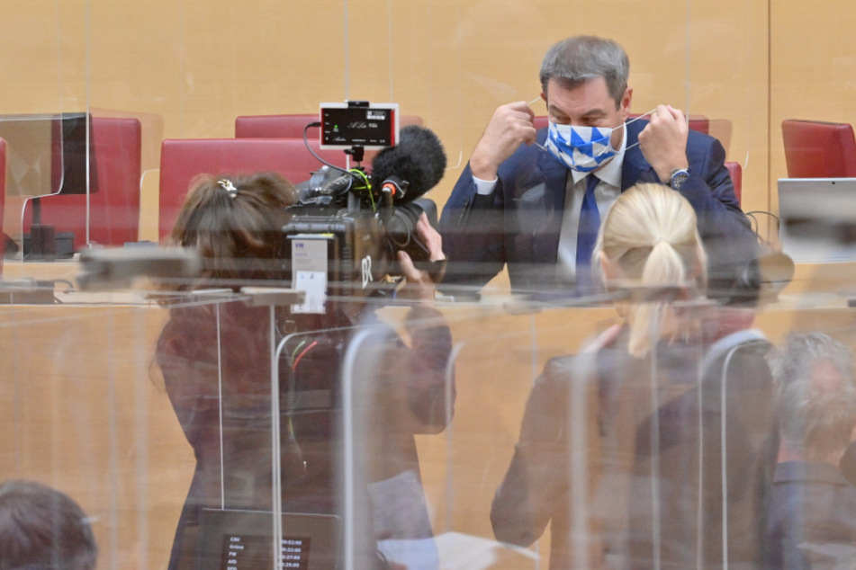 Markus Söder (CSU), Ministerpräsident von Bayern, setzt sich vor Beginn der Sitzung des bayerischen Landtags hinter einer Plexiglasabtrennung seinen Mund-Nasen-Schutz auf.