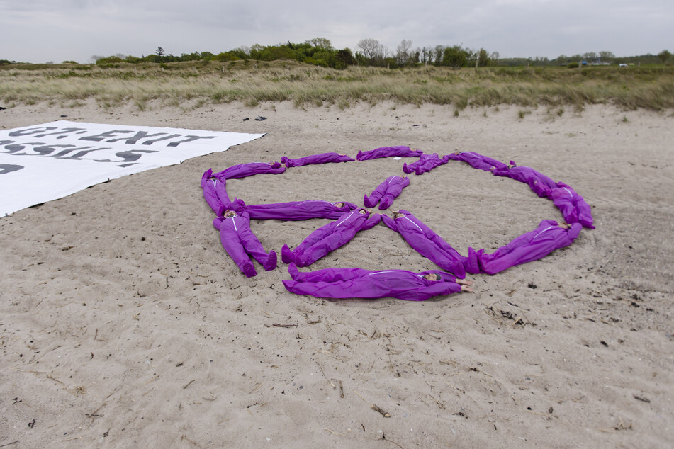 Ein Banner der Umweltaktivisten Greenpeace mit der Aufschrift "G7: Exit Fossils Enter Peace" und eine Gruppe von Aktivisten liegen während des Gipfeltreffens der Außenminister der G7-Gruppe am Strand von Wangels.