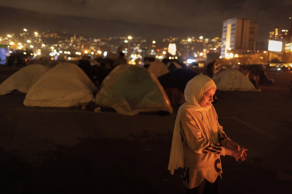 An orphaned girl stands next to a fire outside a tent at a temporary encampment for displaced people in Beirut, Lebanon, on March 30, 2026.
