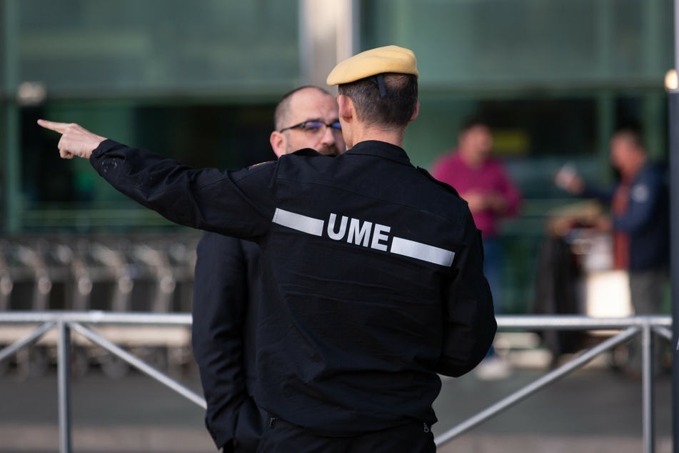 Ein Mitarbeiter der militärischen Notstandseinheit (EMU) der Armee gibt einem Mann Anweisungen bei dessen Ankunft am Flughafen El Prat.