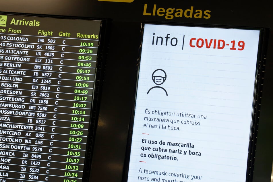 Anzeigetafeln zeigen die ankommenden Flüge am Flughafen von Palma de Mallorca und Hinweise zum Tragen von Mund-Nasen-Schutz im Gebäude an.