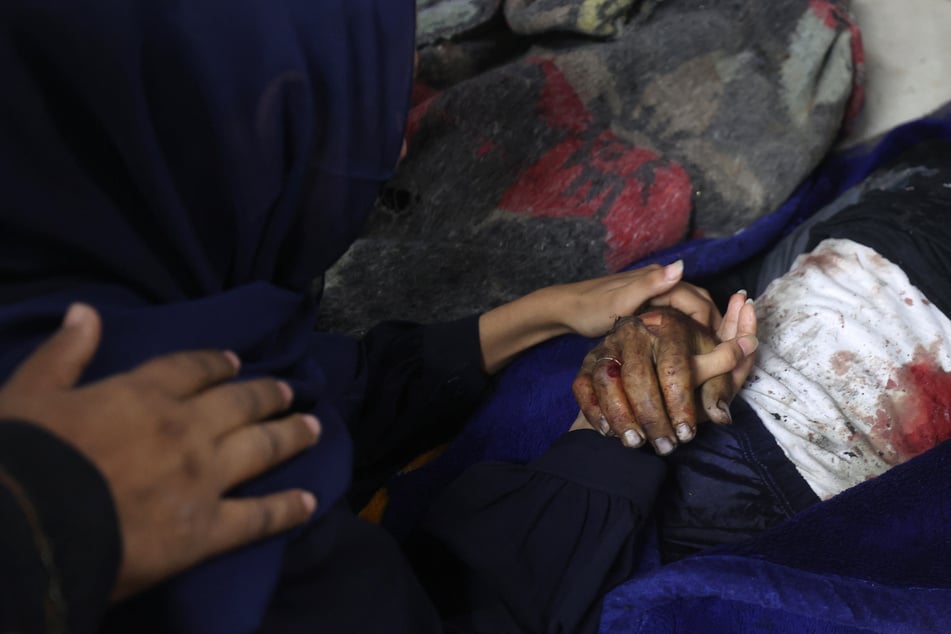 A Palestinian woman mourns over the covered body of her husband, killed in an Israeli strike near the Nuseirat refugee camp, at the al-Awda Hospital in the central Gaza Strip, on September 24, 2025.