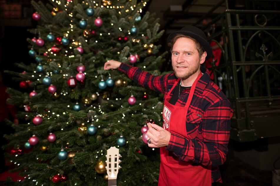 Johannes Oerding schmückt einen Weihnachtsbaum im Rahmen der Aktion "Mehr als eine warme Mahlzeit".