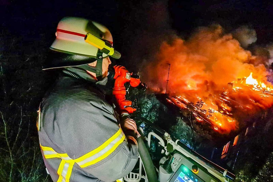 Ein Feuerwehrmann steht auf einer Drehleiter und verschafft sich von oben einen Überblick über das Brandgeschehen.