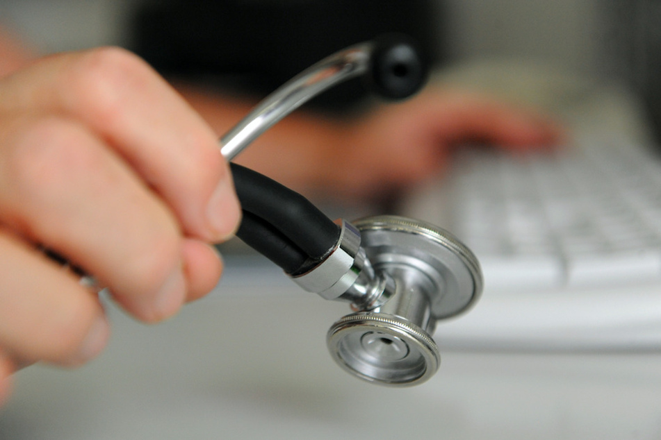 Ein Arzt hält in einem Behandlungszimmer in seiner Praxis ein Stethoskop in der Hand, mit der anderen Hand bedient er eine Computertastatur. (Symbolbild)