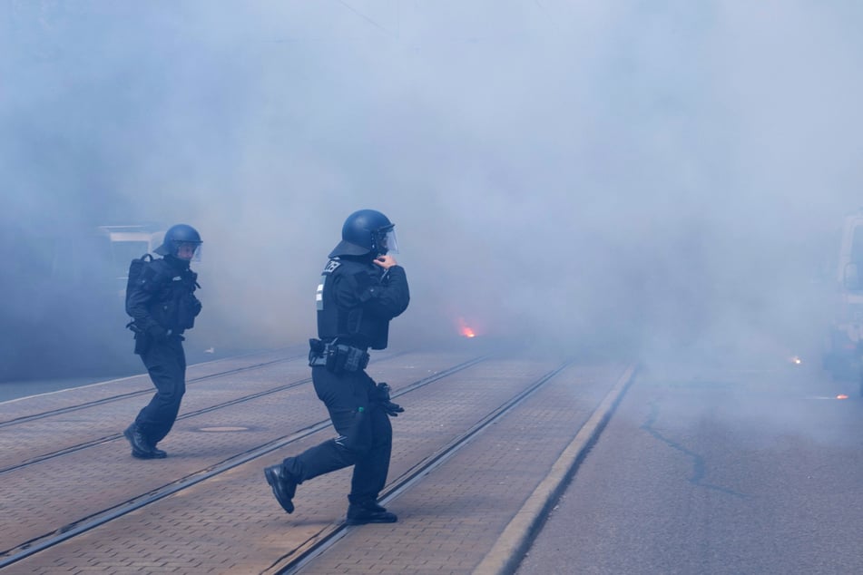 Zwei Polizisten laufen im Nebel von Pyrotechnik vor dem Stadion entlang.