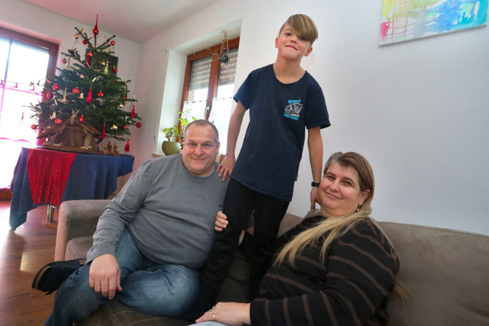 Alexander Merz (l.) und seine Frau Gisela Merz sitzen gemeinsam mit ihrem 10-jährigen Pflegekind Alois in ihrem Wohnzimmer.